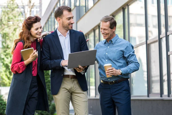 Empresários sorridentes com café para ir e diário trabalhando em conjunto com laptop — Fotografia de Stock