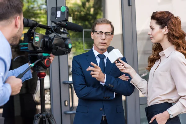 Caméraman professionnel et journaliste de nouvelles parlant avec un homme d'affaires sérieux — Photo de stock