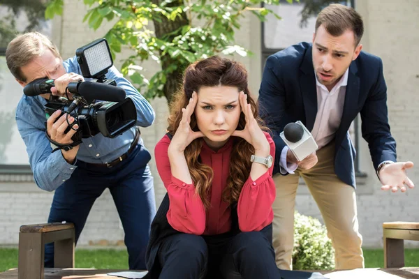 Cameraman with digital video camera and male newscaster with microphone talking to tired businesswoman — Stock Photo