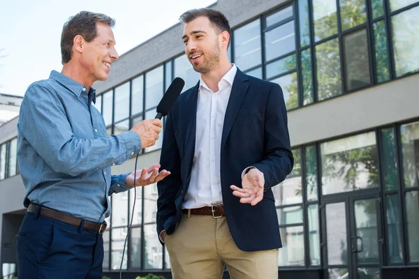 Profesional madura periodista entrevistando exitoso hombre de negocios con micrófono - foto de stock