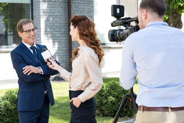 Camarógrafo profesional y periodista entrevistando alegre hombre de negocios - foto de stock