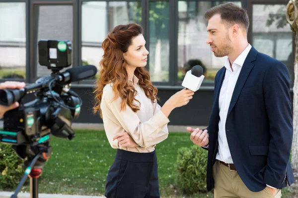 Beautiful serious female news reporter taking interview with businessman — Stock Photo