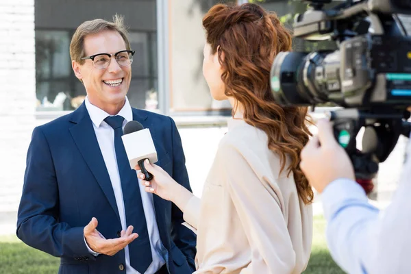 Cameraman with video camera and anchorwoman interviewing successful businessman — Stock Photo