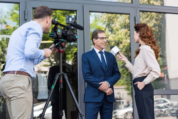 Cameraman and news anchor interviewing businessman near office building — Stock Photo