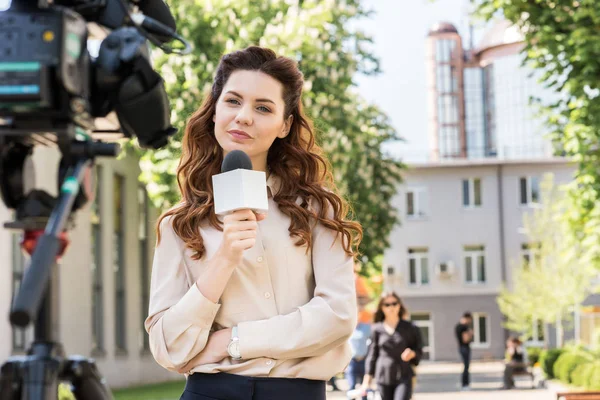 Attractive serious news reporter with microphone looking at digital video camera — Stock Photo