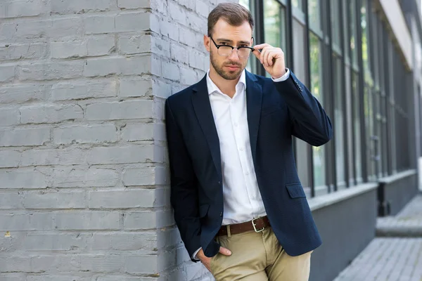 Confiado hombre de negocios con estilo en gafas que posan cerca del edificio de oficinas - foto de stock