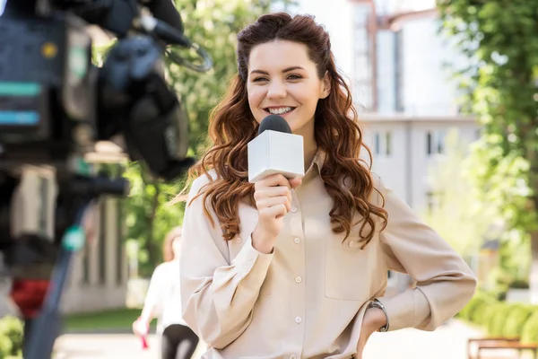 Attraente giornalista sorridente femminile con microfono che parla con videocamera digitale — Foto stock