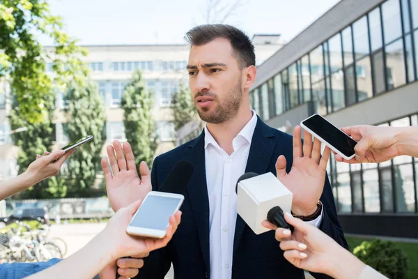 Journalists interviewing serious businessman with microphones and smartphones — Stock Photo