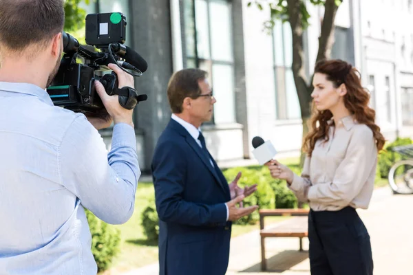 Selective focus of professional cameraman with digital video camera and news reporter interviewing executive businessman — Stock Photo