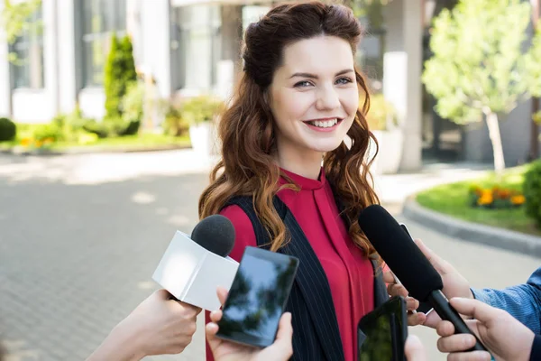 Journalists interviewing public successful businesswoman with microphones and smartphones — Stock Photo