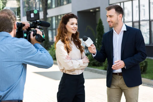 Cinegrafista profissional e repórter de notícias do sexo masculino entrevistando sorridente empresária — Fotografia de Stock