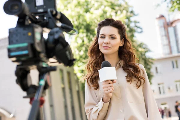 Beautiful female journalist with microphone talking to digital video camera — Stock Photo