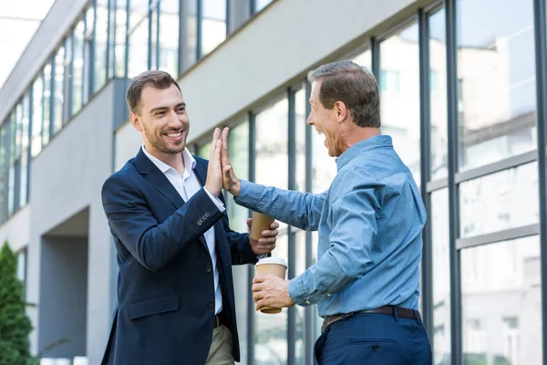 Business colleagues with coffee to go giving high five near office building — Stock Photo