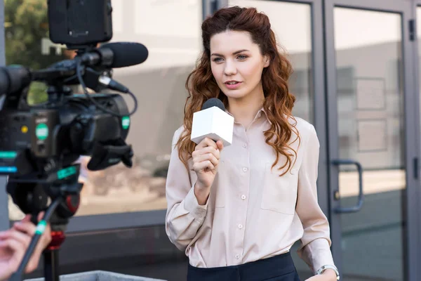 Confident anchorwoman with microphone standing in front of digital video camera — Stock Photo