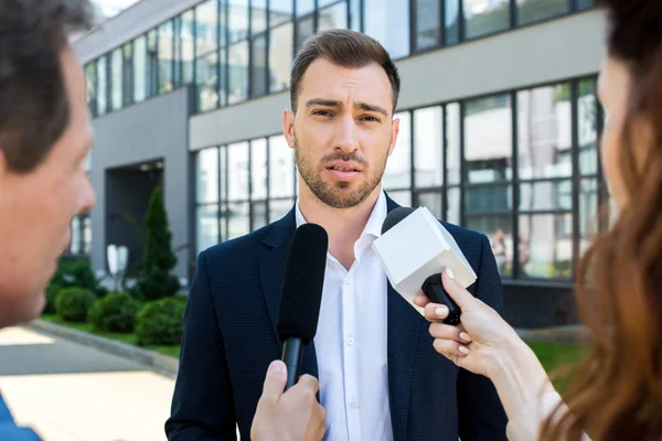 Two professional journalists interviewing businessman with microphones — Stock Photo