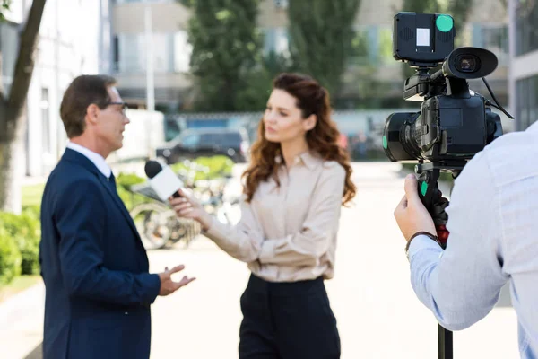 Cameraman and anchorwoman with microphone interviewing businessman — Stock Photo
