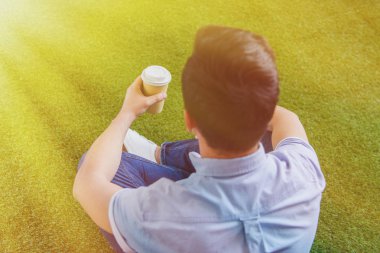 young man sitting on grass with cup on coffee to go clipart