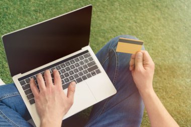 kırpılmış çim üzerinde otururken e-defter ile alışveriş yapma genç adam kadeh