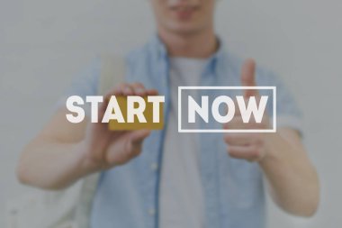 cropped shot of young man holding golden card and showing thumb up with start now inscription on foreground clipart