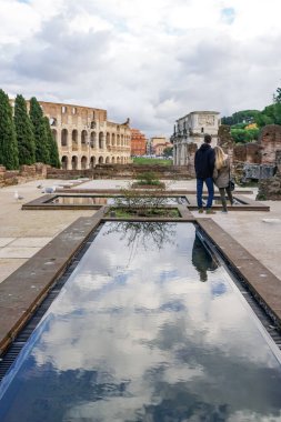 ROME, ITALY - APRIL 10, 2020: back view of man and woman standing near ancient colosseum and historical buildings  clipart