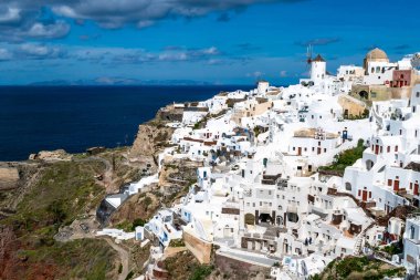 Santorini 'deki bulutlu gökyüzüne karşı durgun deniz kenarında beyaz evler 