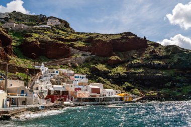 SANTORINI, GREECE - 10 Nisan 2020: Ege Denizi yakınlarındaki tepenin üzerindeki beyaz evler bulutlu gökyüzüne karşı 