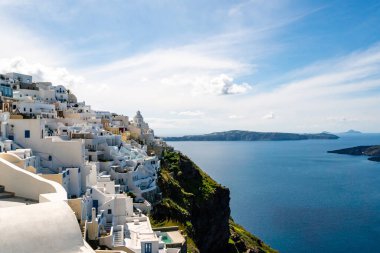 sunshine on white houses near tranquil aegean sea against sky with clouds in Santorini clipart