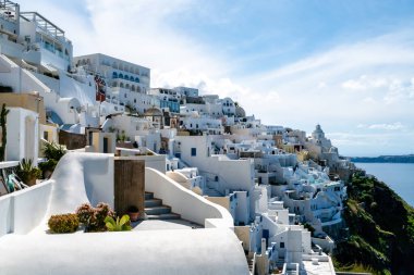 SANTORINI, GREECE - 10 Nisan 2020: sakin Ege Denizi yakınındaki beyaz evler bulutlu gökyüzüne karşı