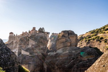 sunlight on orthodox monastery on rock formations against blue sky in meteora  clipart