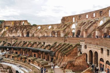 ROME, ITALY - APRIL 10, 2020: people near ruins of historical colosseum against cloudy sky  clipart