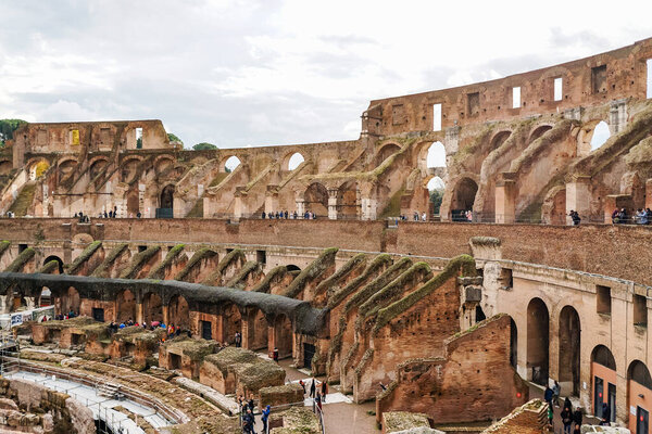 ROME, ITALY - APRIL 10, 2020: people near ruins of historical colosseum against cloudy sky 