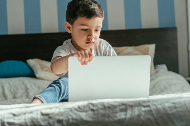 Yatak odasında dizüstü bilgisayar kullanan küçük çocuğun seçici odak noktası 