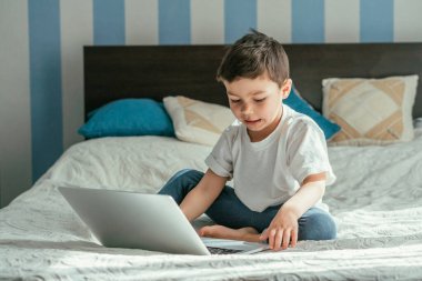 Yatak odasında dizüstü bilgisayar kullanan sevimli çocuğun seçici odağı. 