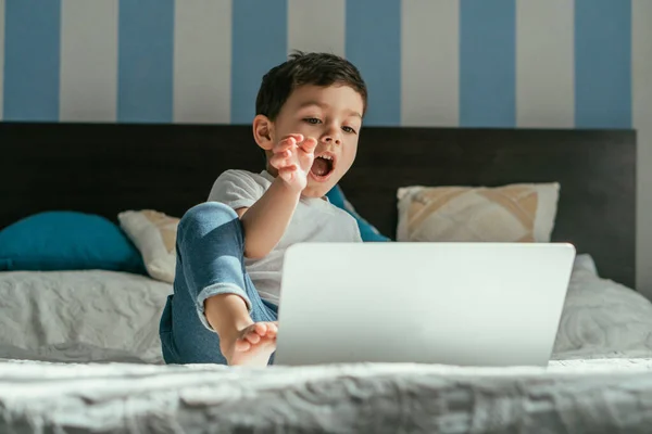 Selective Focus Emotional Toddler Boy Gesturing While Looking Laptop Bedroom — Stock Photo, Image