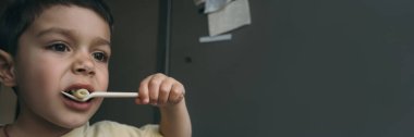 Çatalla makarna yerken yemek yiyen sevimli çocuğun yatay görüntüsü.