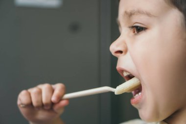 Çatalla makarna yerken yemek yiyen sevimli çocuğun yan görüntüsü.