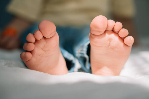 selective focus of barefoot feet of cute boy on bedding 