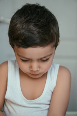 Düşünceli esmer çocuk, cübbeli, eğik başıyla oturuyor.