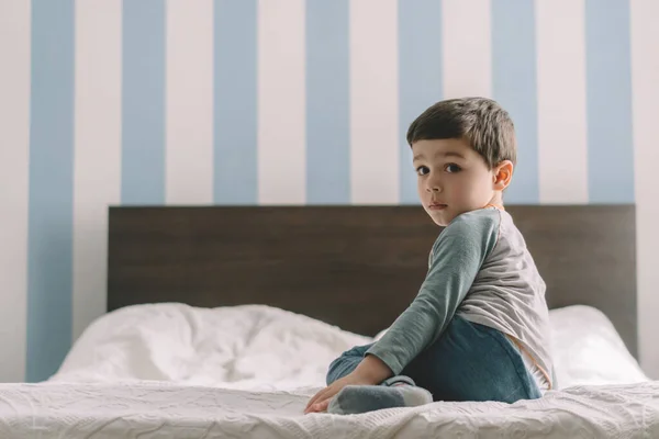 Niedlicher Ernsthafter Junge Schaut Die Kamera Während Hause Bett Sitzt — Stockfoto