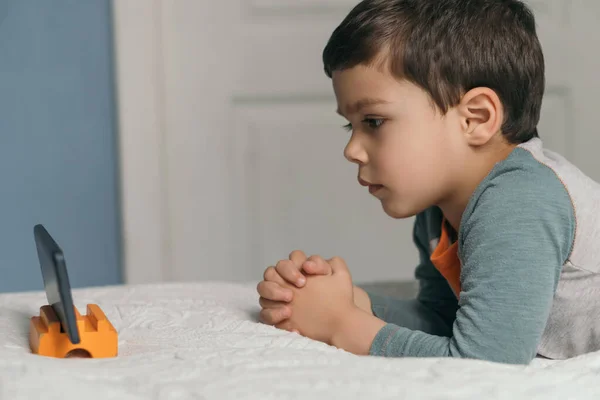 Özenli, tatlı bir çocuğun yatakta uzanıp akıllı telefondan eğitici çizgi film izlemesi.