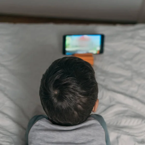 Felső Nézet Fiú Néz Oktatási Rajzfilm Okostelefon Miközben Fekszik Ágyban — Stock Fotó