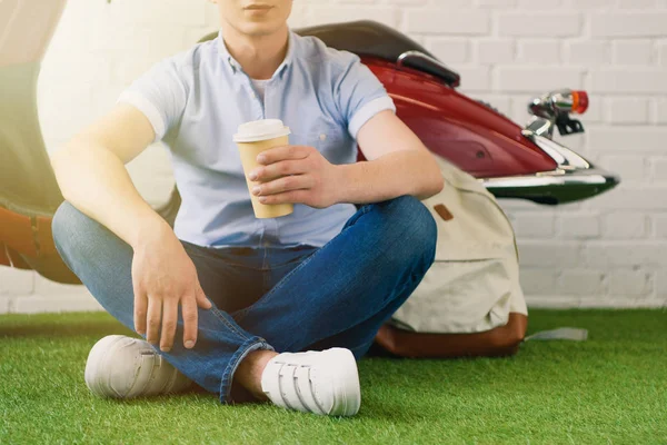 Cropped shot of young man with cup of coffee to fo sitting in front of vintage scooter — Stock Photo