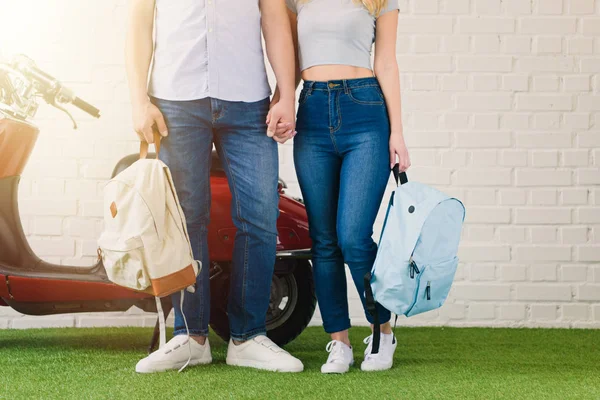Tiro cortado de casal com mochilas de mãos dadas na frente de scooter vintage — Fotografia de Stock
