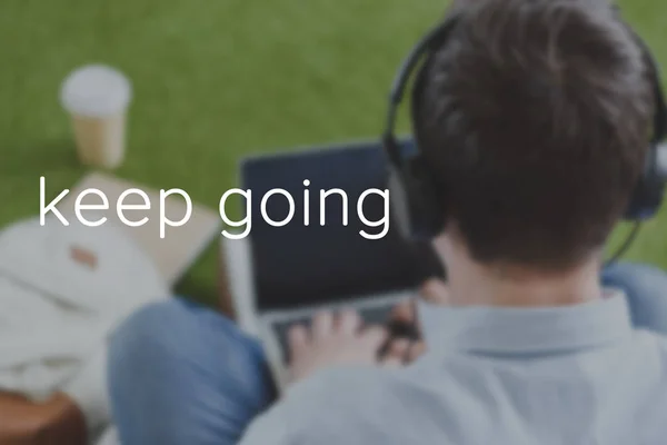 Close-up shot of man in headphones using laptop, keep going inscription — Stock Photo