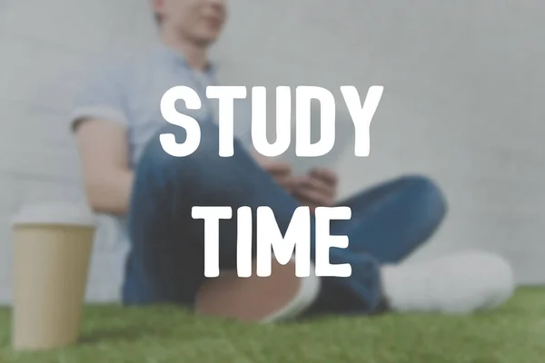 Cropped shot of young man sitting on grass and using tablet, study time inscription — Stock Photo