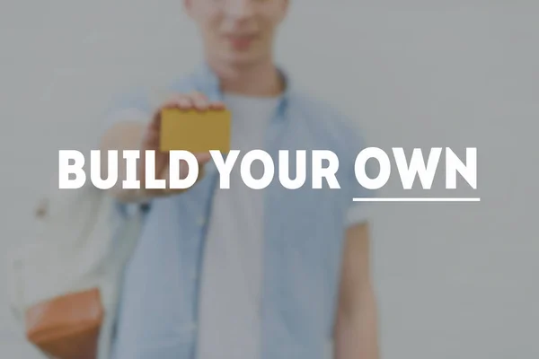 Cropped shot of young man holding golden card with build your own inscription on foreground — Stock Photo