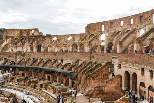 ROMA, ITALIA - 10 DE ABRIL DE 2020: personas cerca de las ruinas del coliseo histórico contra el cielo nublado - foto de stock