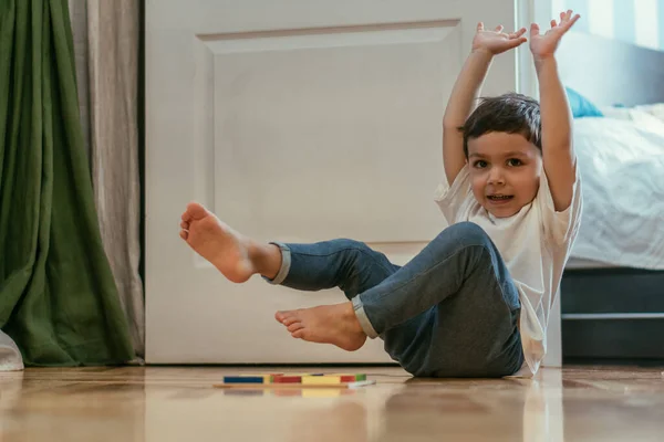 Selective focus of cute toddler boy with hands above head near toys on floor — Stock Photo