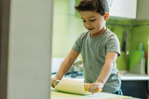 Messa a fuoco selettiva del ragazzo bambino felice che tiene il mattarello vicino alla pasta cruda sulla carta da forno — Foto stock