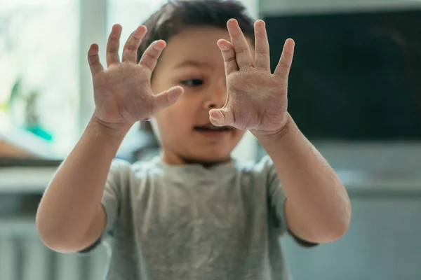 Селективный фокус милого мальчика, показывающего руки в муке дома — стоковое фото
